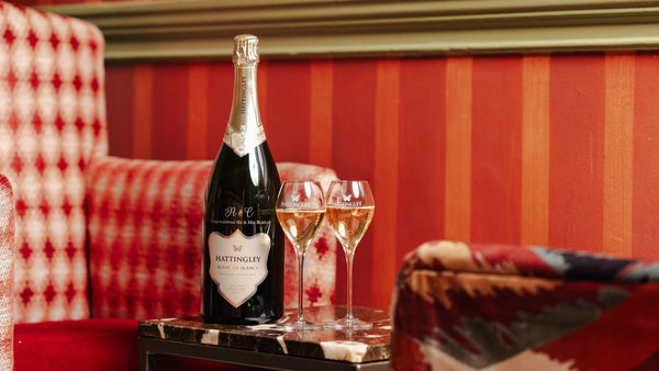 Hattingley Valley Blanc de Blancs Magnum Bottle with engraved personalisation, filled glasses tulip flutes beside it on a table with a luxurious hotel background