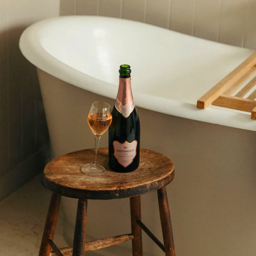 Bottle of Hattingley Valley English Sparkling english champagne and a glass on a wooden stool in front of a bathtub.