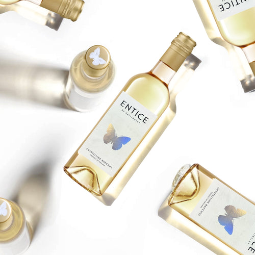 Case of Six Gold and white Entice 2025 bottles with silver butterfly design. Bottles at different angles casting shadows on a white background.