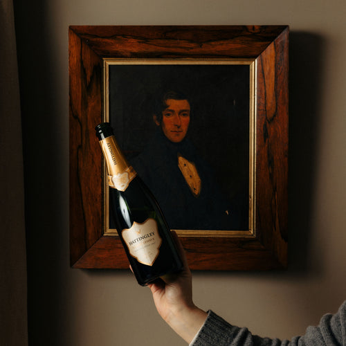 A bottle of Classic Reserve is held in front of wooden and golden framed vintage portrait.