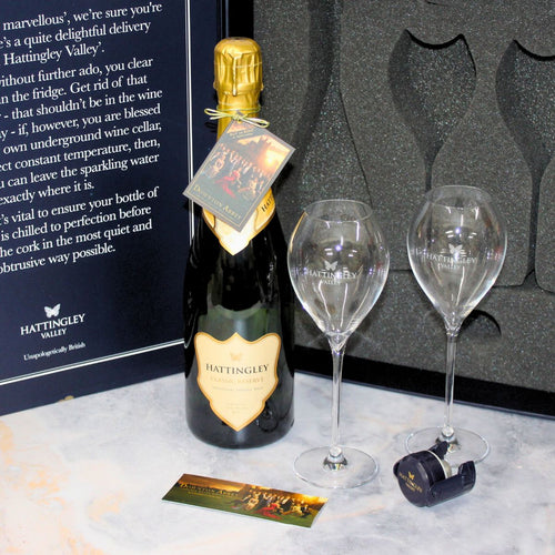 Open Luxury Gift set on a marble counter top with a pair of Hattingley valley branded tulip flutes and a sparkling wine bottle stopper in blue, included is a invitation to watch the new movie Downton Abbey: The Grand Finale at home.