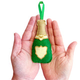 Green felt champagne bottle ornament held in hands against a white background
