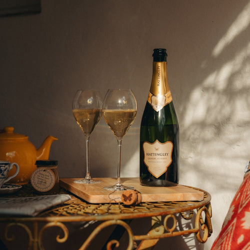 Hattingley Valley English Sparkling Wine and two glasses on a wooden tray with a teapot in the background.