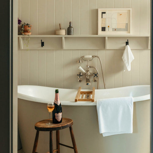 Bathroom with a bathtub, bottle of English Sparkling Rosé, and glass on a stool beside.