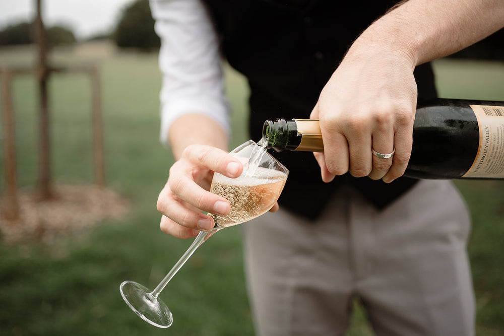 Image of groom pour a glass of wine on his wedding day, traditional method English Sparkling wine, Hattingley Valley award winning wines