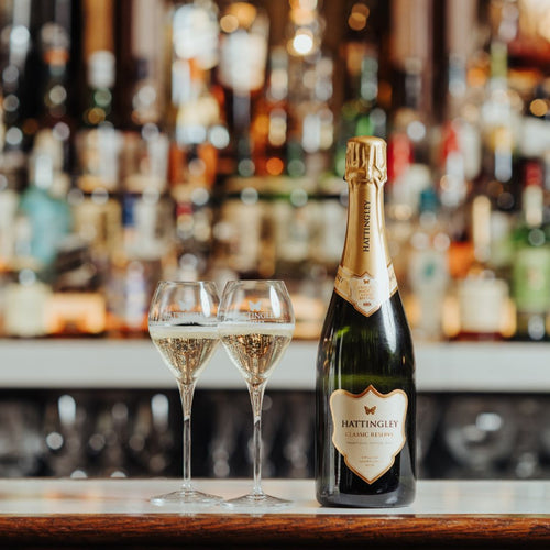 Classic Reserve lifestyle image, Bottle with two filled glasses on the hotel bar, bubbles fizzing in the glasses. Luxury hotel bar background slightly blurred with alcohol bottles lining the shelves behind.