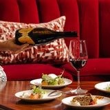 A lifestyle image of someone pouring a glass of Hattingley Valley STILL Pinot Noir with a luxurious set in the background and various plates of food in the foreground