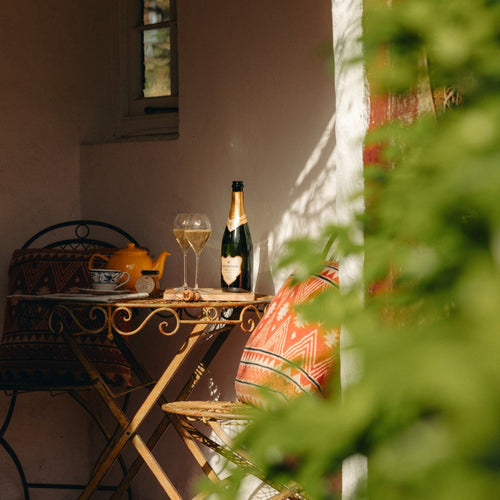 Bottle of Hattingley English Sparkling Wine and glasses on a table with a teapot, surrounded by greenery.