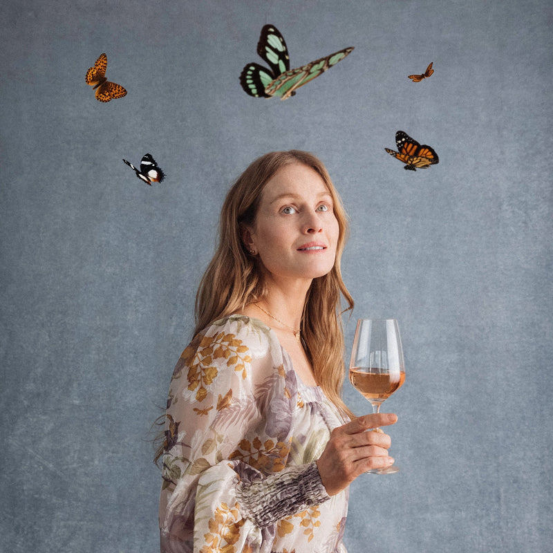 Hattingley Valley lifestyle image, lady holding a glass of sparkling Rosé looking up at a cluster of butterflies around her head 