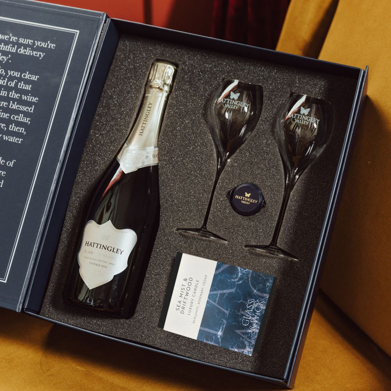 Hattingley Valley Luxury gift set with candle lifestyle image, Hattingley valley award winning Blanc de Blancs with glass tulip flutes, wine glasses, English Sparkling bottle stopper, Glass & Wick Sea mist and driftwood candle, gifts for her, gifts for him, wine gifts  