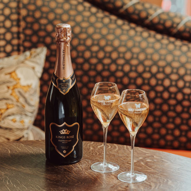 Lifestyle image of the Hattingley Valley Kings Rosé premium sparkling wine, image of filled flutes on table with Rosé bottle beside, with luxurious hotel background