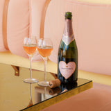 Hattingley Valley Valentine's Day Rosé, premium English Rosé with Limited Edition heart label, gifts for Valenitine's, image open bottle on refelctive table with two Hattingley glass flutes filled with rosé beside, Joia hotel pink background