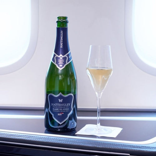 Bottle of Hattingley Valley Blanc de Noirs for British Airways on board British Airways Club World Cabin on Windowsill aeroplane windows in the background. Filled champagne flute beside the bottle with English Sparkling bubbling in glass. 