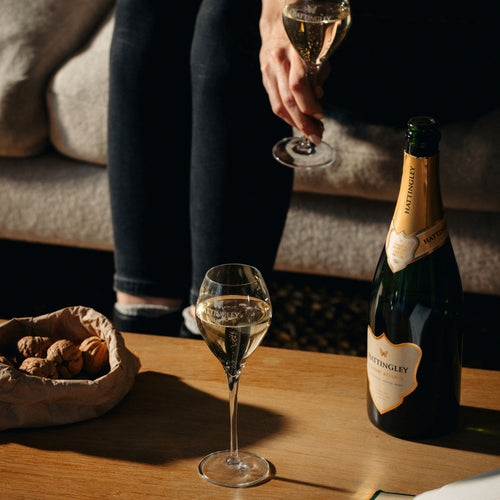 A cozy scene with english sparkling wine flutes, a bottle of classic reserve from hattingley valley, and walnuts on a wooden table.