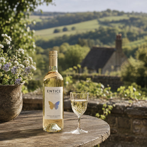Bottle of Entice white wine with a glass on a wooden table in a scenic outdoor setting.