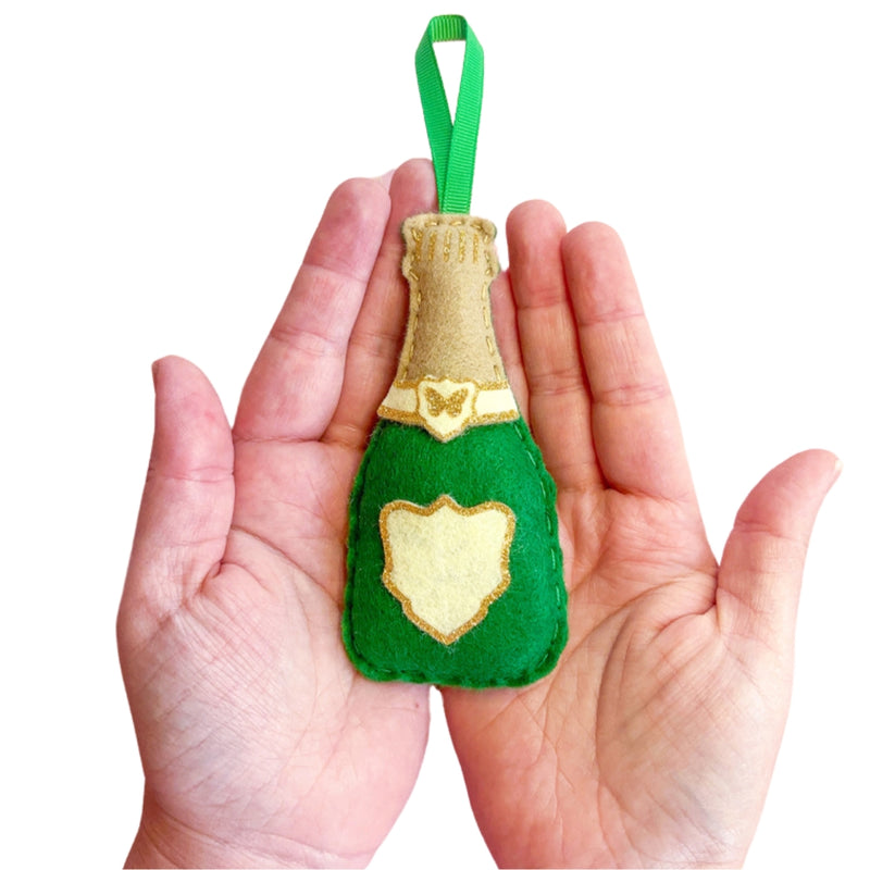 Green felt champagne bottle ornament held in hands against a white background