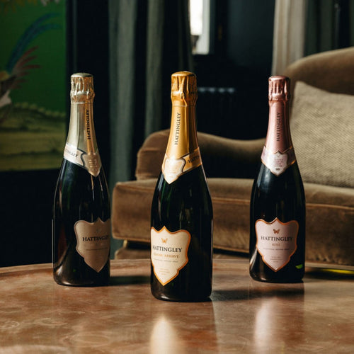Three bottles of Hattingley sparkling wine on a wooden table with a blurred background