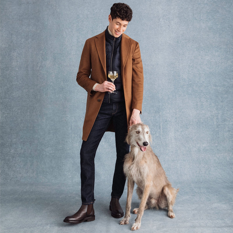 Lifestyle image: a gentleman holding a champagne glass of Hattingley Valley Classic reserve, premium English sparkling wine, in one hand. In the other he is holding a lurcher dog by the collar and smiling down at it