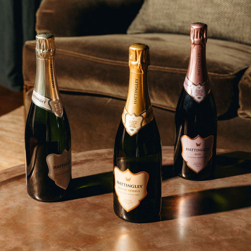 Three bottles of Hattingley sparkling wine on a wooden surface with a blurred background.