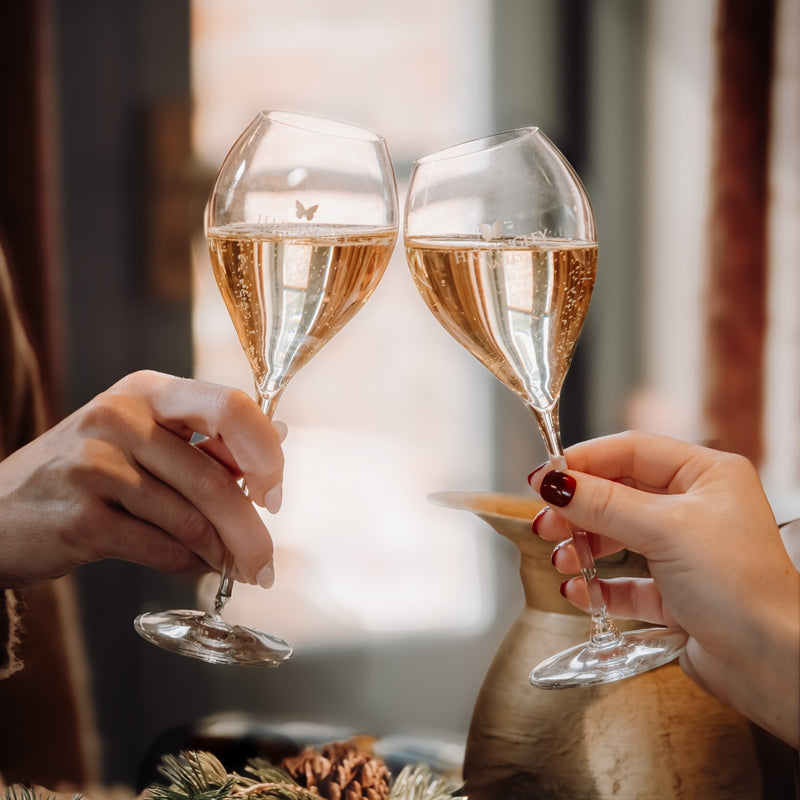 Hattingley Valley Tulip glass flutes cheer-sing with English sparkling wine. Festive christmas table in the background. glasses have a tulip shape and a Hattingley valley logo on them with a gold butterfly/