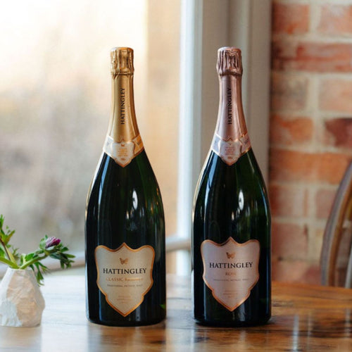 Magnum of Classic Reserve NV, Magnum of Rosé on a wooden surface, with a flower vase beside and a window and brick wall in the background.