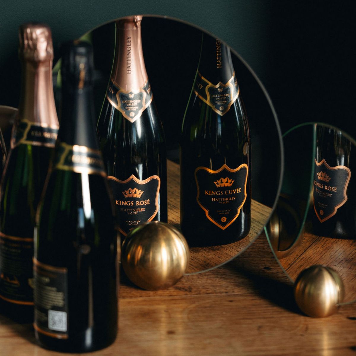 A bottle of Kings Cuvée and Kings Rosé reflected in two small mirrors on a desk, close up of the wine labels.