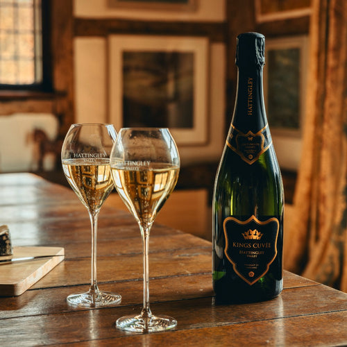 Two glasses of Hattingley Valley Prestige English Sparkling wine King's Cuvée on a wooden table.