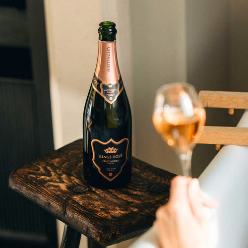 Bottle of Kings Rose English Sparkling Wine on a wooden stool with a glass of champagne in the foreground.