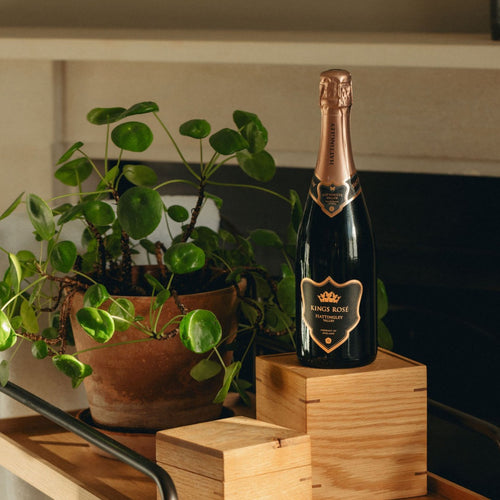 Bottle of Kings Rose English Sparkling Wine on a wooden block with a plant in the background