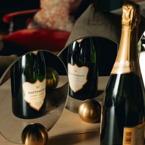 A bottle of Classic Reserve is reflected in two mirrors, complemented by gold accents and a cozy setting with a red, cushion filled chair in the background.