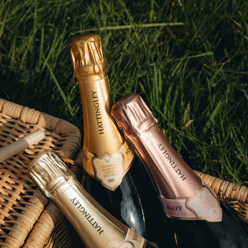 Three bottles of Hattingley Valley English Sparkling Wine in a picnic basket on a grassy background