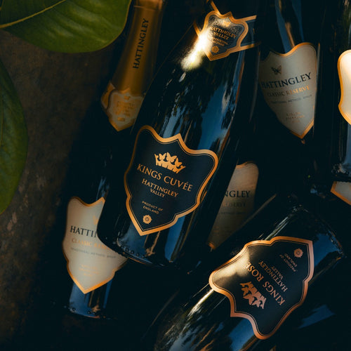 Hattingley Kings Cuveé and multiple Hattingley Valley English Sparkling bottles with gold labels piled atop of one another.