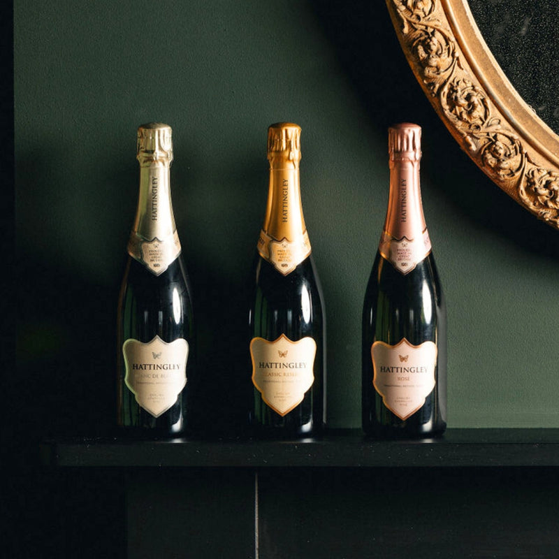 Three bottles of Hattingley English Sparkling Wine on a dark surface with a decorative mirror in the background. Christmas Sparkle Trio Bundle.