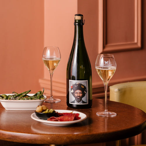 A bottle of the English Gent English Sparkling Wine on a table with charcuterie, padron peppers and two poured glass flutes