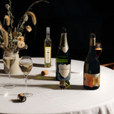 Lifestyle image of three Hattingley valley wines on a autumnal table, Blanc de Blancs English sparkling, still chardonnay and Entice dessert wine. Bottles casting a dark shadow on the white table cloth.