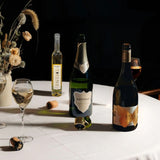 Lifestyle image of three Hattingley valley wines on a autumnal table, Blanc de Blancs English sparkling, still chardonnay and Entice dessert wine. Bottles casting a dark shadow on the white table cloth.