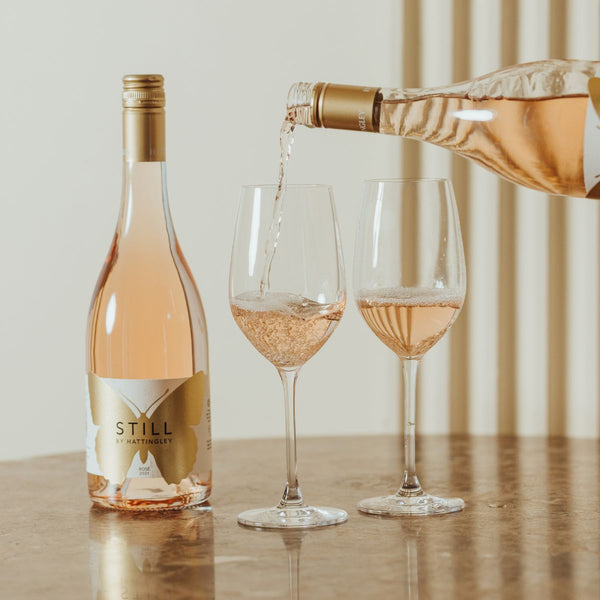 A lifestyle image of someone pouring a bottle of Hattingley Valley STILL Rosé with two glasses in view on a marble table top 