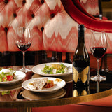 Lifestyle image of our Hattingley Valley Pinot Noir, Bottle and filled glasses on a table with delicious food pairings, luxurious hotel background furnishings. Finest English wine, Top English Still Wines