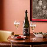 Lifestyle image, Hattingley Valley, The English Gent sparkling wine, image of filled flutes next to a bottle on a restaurant table with plates of tapas style food