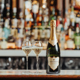 Classic Reserve lifestyle image, Bottle with two filled glasses on the hotel bar, bubbles fizzing in the glasses. Luxury hotel bar background slightly blurred with alcohol bottles lining the shelves behind.