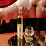 Entice English Dessert Wine, lifestyle image, bottle and glass on a reflective table with a luxurious hotel background. Bacchus grape wine, English sweet wine.