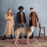 Hattingley Valley Lifestyle Image, three people standing with a greyhound in front of them. The lady on the left is holding a bunch of tulips, the Gent in the middle has a butterfly on his shoulder, the Gent on the right is holding a glass of Hattingley sparkling wine.