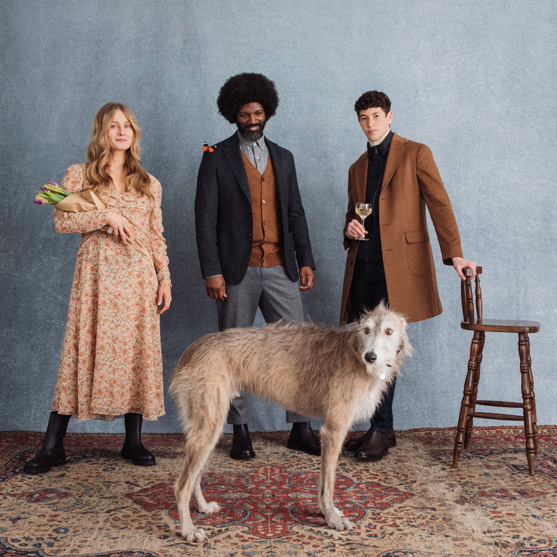 Hattingley Valley Lifestyle Image, three people standing with a greyhound in front of them. The lady on the left is holding a bunch of tulips, the Gent in the middle has a butterfly on his shoulder, the Gent on the right is holding a glass of Hattingley sparkling wine.